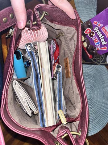 Open handbag filled with items like a notebook, planner, mini frosted donuts, wallet, hand sanitizer, pen, and hair clip