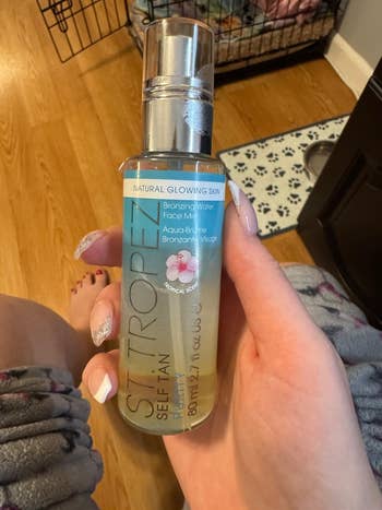 Person holding a vessel of St. Tropez Self Tan Purity Bronzing Water Face Mist with a floral label