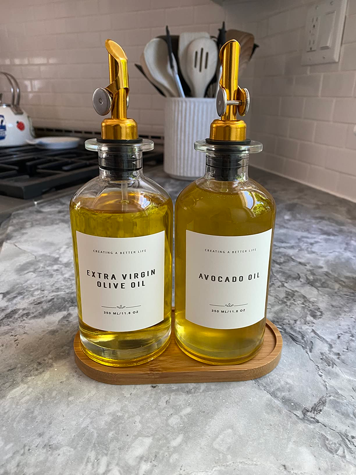 reviewer's two oil dispensers on the bamboo tray with avocado oil and extra virgin olive oil labels applied