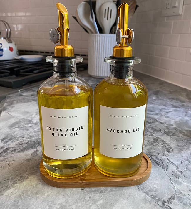 reviewer's two oil dispensers on the bamboo tray with avocado oil and extra virgin olive oil labels applied