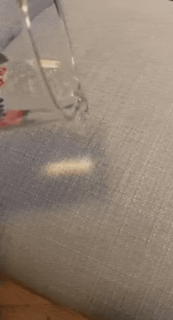Reviewer pouring water on their couch after applying the repellant spray and showing the water just slide off the fabric