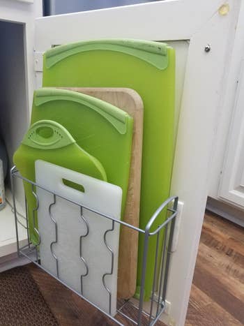 reviewer's cutting boards mounted in the holder inside a cabinet door using command hooks