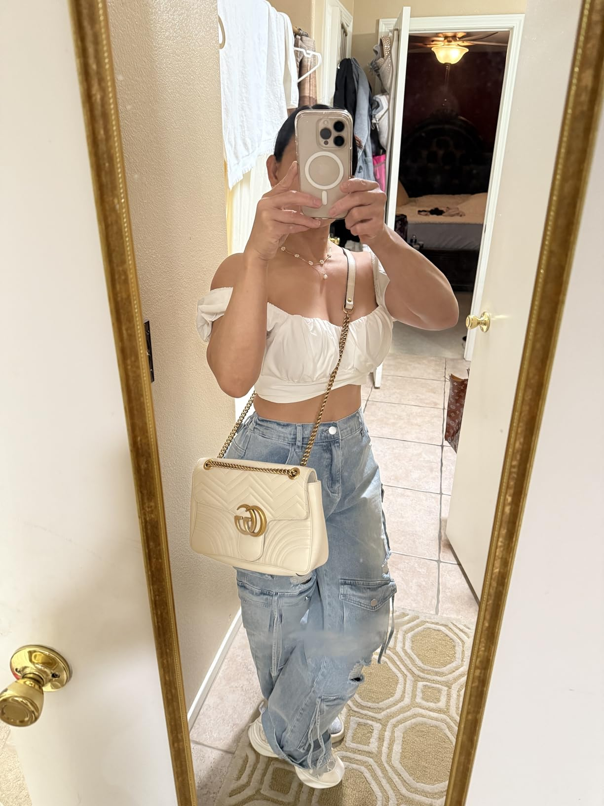 Person taking a reflector  selfie wearing a achromatic  off-shoulder top, distressed jeans, and holding a quilted decorator  handbag with a concatenation  strap