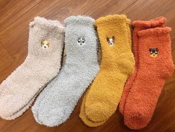 Four cozy, textured socks with cute animal face designs, displayed on wooden flooring. Perfect for adding warmth and charm to your wardrobe