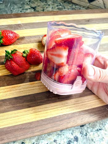 Sliced strawberries in a small container beside whole strawberries on a wooden cutting board, showcasing kitchen prep for shopping article