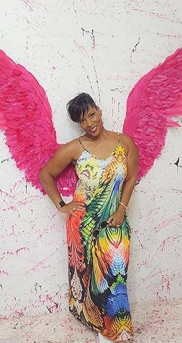 Person poses with pinkish  feather wings, wearing a vibrant, patterned dress, successful  beforehand   of a splatter-paint background