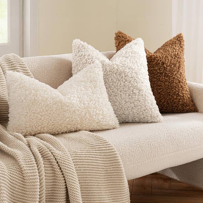 Three textured throw pillows in cream and brown on a cushioned sofa with a knitted blanket, showcasing cozy home decor options