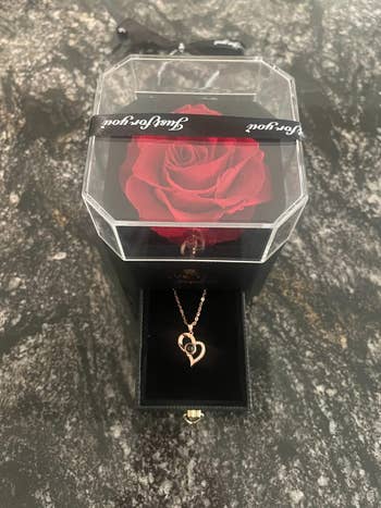 a reviewer image of a rose on top of a box that holds a gold heart shaped necklace