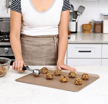 someone scooping evenly-sized balls of cookie dough onto a baking sheet