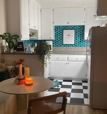 a reviewer's kitchen interior with white cabinets, checkered floor, and teal backsplash. Table with chair in the foreground. No people