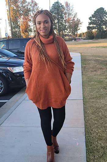 reviewer wearing the orange sweater dress with black leggings and boots