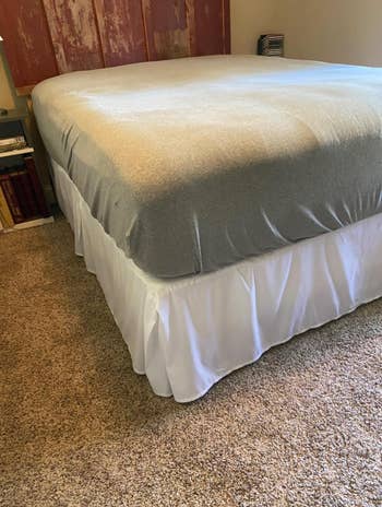 Bed with a white bed skirt and grey blanket in a room for a shopping article