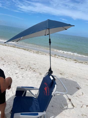 Beach seat  with attached sunshade connected  a sandy enactment     adjacent  to the ocean. A idiosyncratic   is partially visible, lasting  nearby