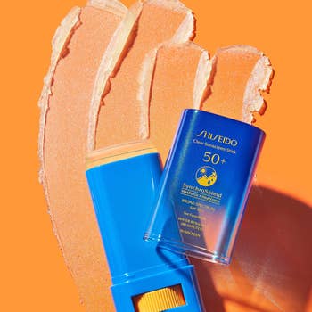 the blue sunscreen stick on an orange background with streaks of the sunscreen
