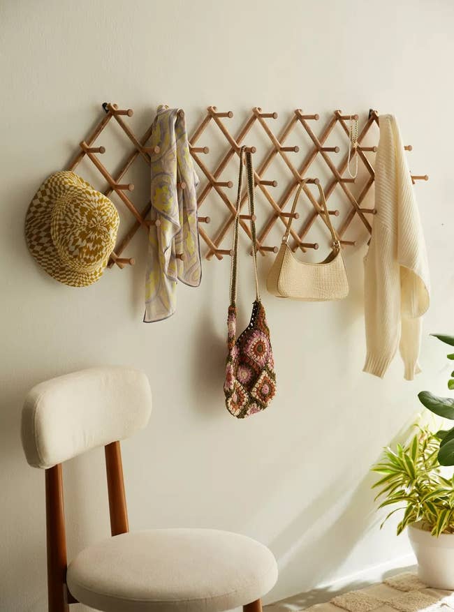 wall-mounted wooden lattice hanger with bags, scarf, and hat; adjacent to a chair