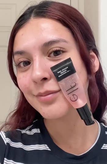 Person holding a conduit of e.l.f. Power Grip Primer adjacent their face, wearing a striped shirt