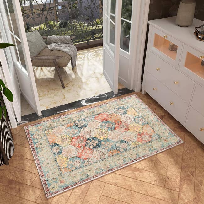 Floral area rug on wooden floor by an open patio with a chair outside, suggesting an inviting space for relaxation