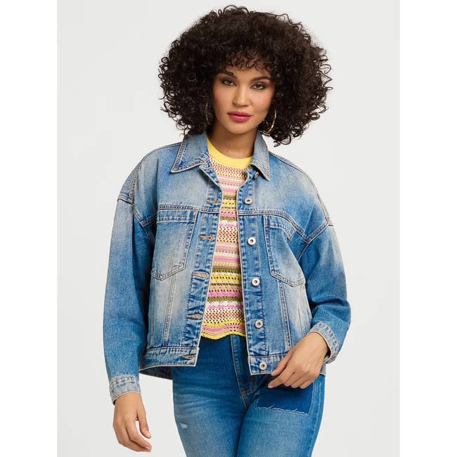 Person wearing a denim jacket over a crocheted top, paired with jeans