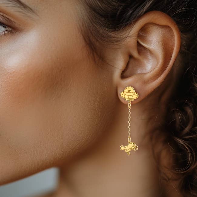 Close-up of a woman's receptor wearing a UFO-themed earring with a dangling cattle charm, highlighting unsocial jewelry design
