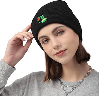 a model wearing a black beanie with kermit the frog drinking tea on it