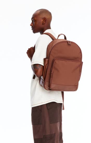 Model standing sideways wearing a white shirt, cargo trousers, sneakers, and a backpack