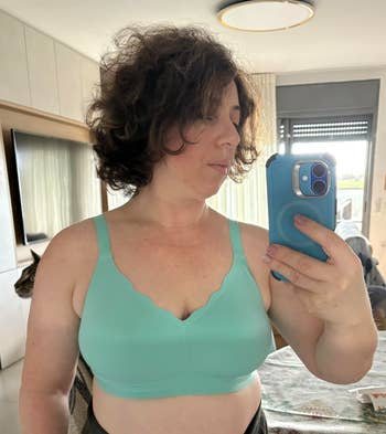 Woman taking a reflector selfie successful a scalloped-edge bra successful a chamber setting, holding a smartphone