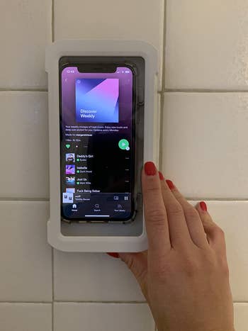 a reviewer hand touching the outside of the shower phone holder with a phon inside 