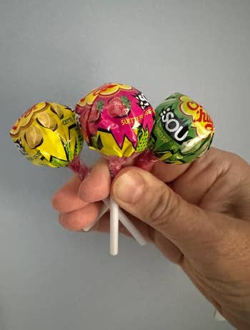 A manus  holding 3  assorted lollipops with colorful wrappers. Perfect for a saccharine  dainty  buying  guide