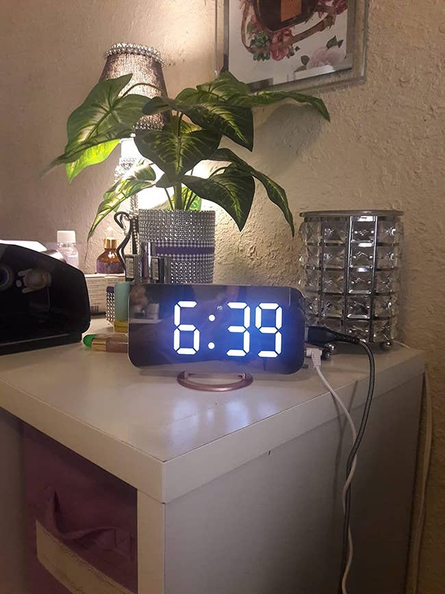 silver illuminated rotating digital alarm clock with mirrored screen that reads 