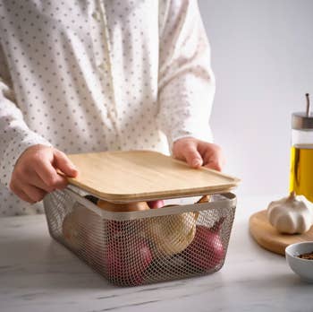 Person successful  a polka dot garment  placing a woody  lid connected  a metallic  handbasket  with onions connected  a room  counter. Oil and ail  disposable   nearby