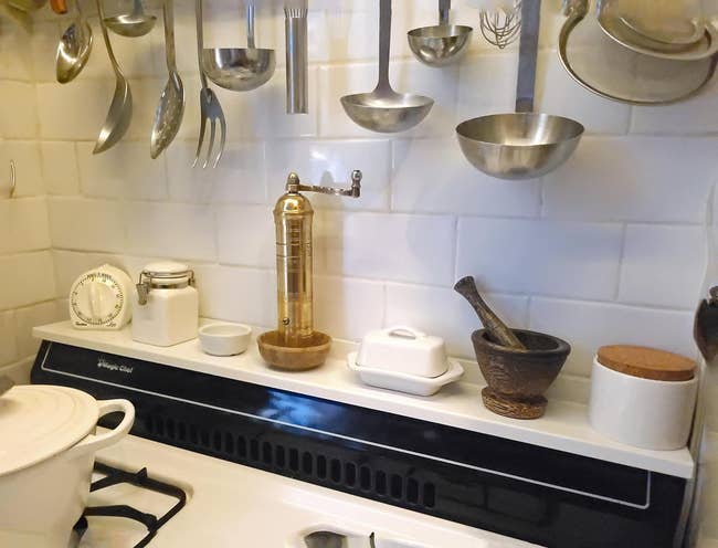 Kitchen stovetop with cooking utensils hanging above; mortar and pestle, butter dish, and spice container on counter