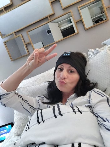 Reviewer under covers wearing black wireless headphones to sleep, while holding up a peace sign