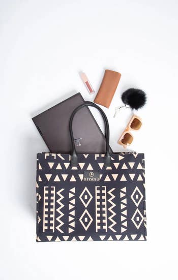 Geometric-patterned tote container with laptop, lipstick, sunglasses, and a tiny leather pouch connected a achromatic surface