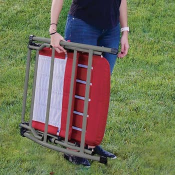 Person standing on grass holding a foldable red chair 