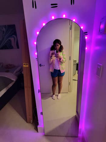 reviewer standing in front of silver arched floor mirror with purple lights behind it