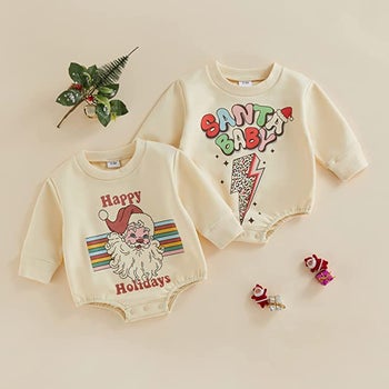 two cream colored long sleeve baby rompers: one says happy holidays and has santa on it and the other says santa baby with a lightnin bolt on it