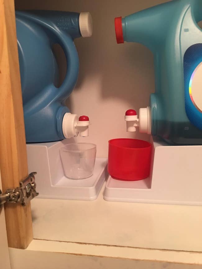 reviewer's cabinet with two of the stands holding large detergent jugs and cups underneath, ready to be filled