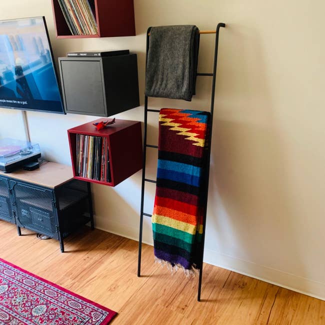 Decorative ladder with a gray blanket and a multicolored woven blanket beside a modern shelving unit in a stylish living space
