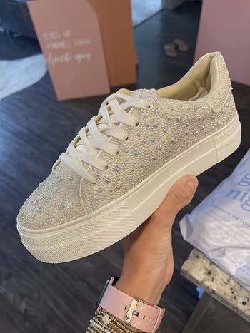 reviewer photo of them holding a rhinestone- and faux pearl-encrusted white sneaker