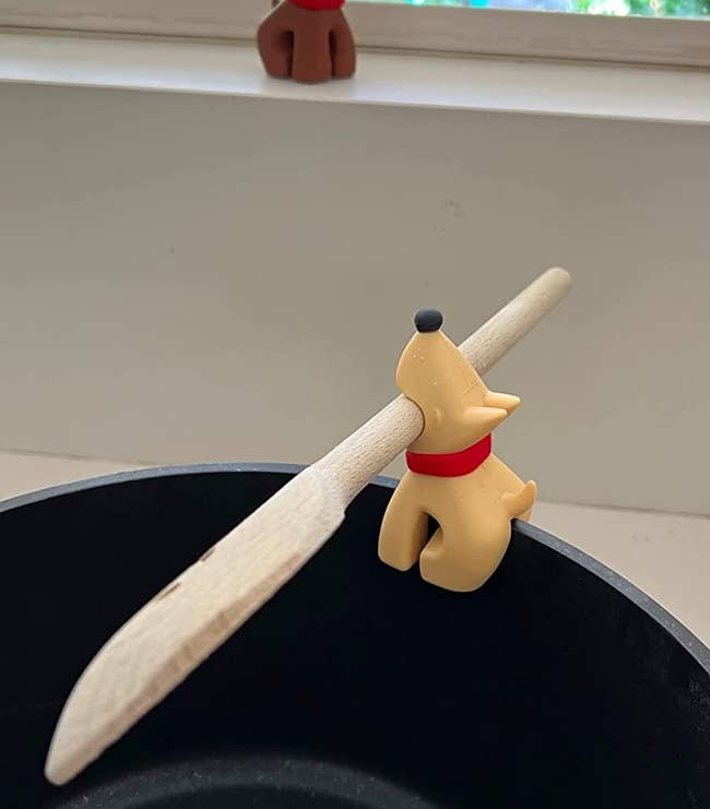 reviewer photo of the dog-shaped silicone lid clip holding a wooden spatula in its mouth