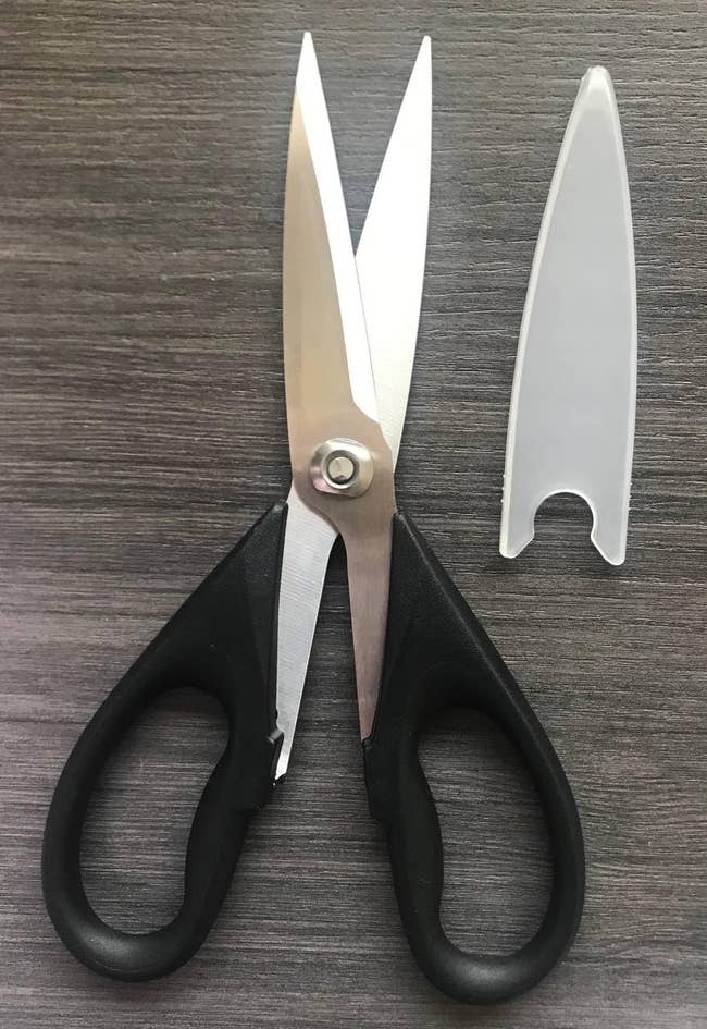 Scissors with achromatic  handles and stainless alloy  blades, shown with a wide   leaf  cover, connected  a grey  surface
