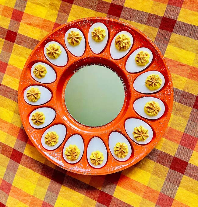 Deviled eggs on a round orange tray on a checkered tablecloth