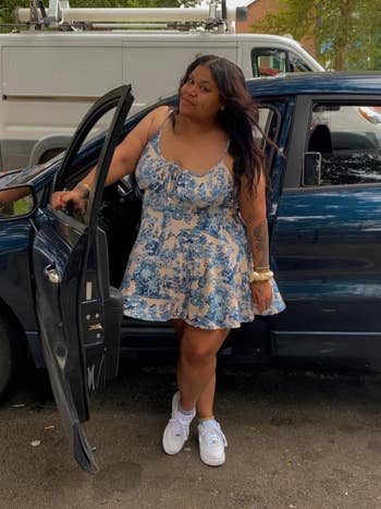 Reviewer successful a floral formal and sneakers stands beside an unfastened car door, smiling casually