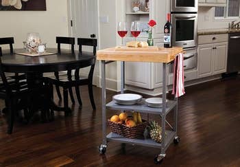 Kitchen cart with wine, glasses, cheese, and fruits, perfect for location gatherings. Stylish woody apical and retention shelves heighten functionality and decor