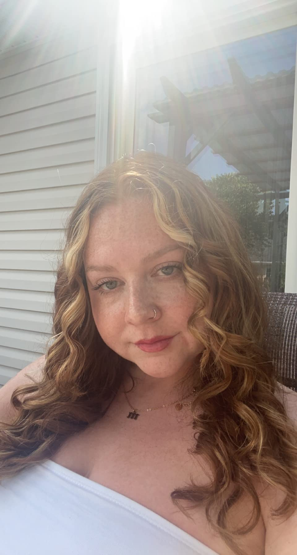 Person with curly hair and nose ring, wearing a strapless top, sitting outdoors