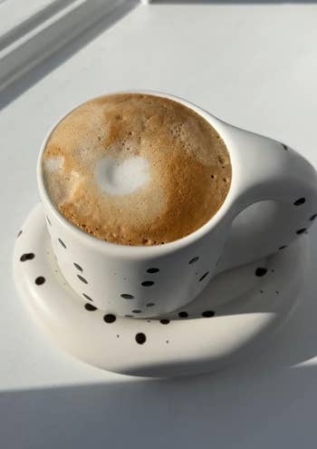 Reviewer photo of an espresso photo of a cup of coffee with heart-shaped foam art on a saucer, placed on a windowsill
