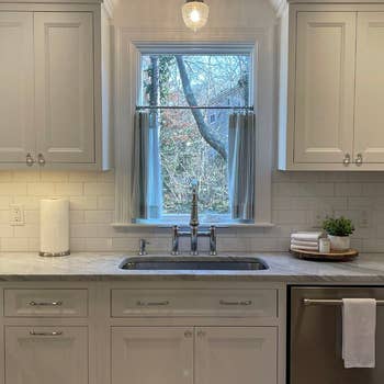 A modern kitchen sink area with white cabinetry, a marble countertop, a stainless steel faucet, a paper towel roll, and a small tray with a plant and candles