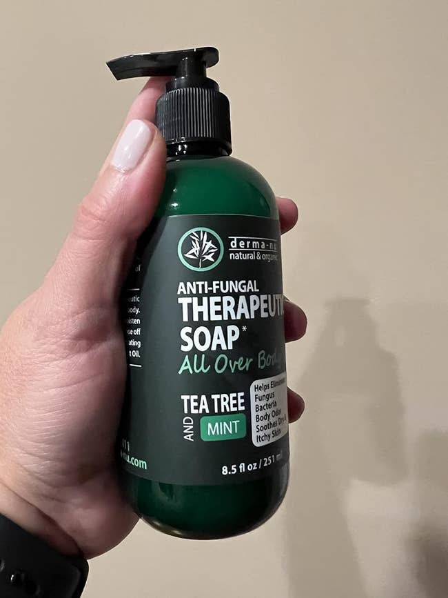 Person holding a bottle of Derma-nu Anti-Fungal Therapeutic Soap with Tea Tree and Mint, emphasizing all-over body use