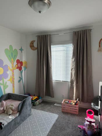 A child’s playroom with toys, a cushioned play   mat, and partition  illustrations of ample  flowers. A model   with curtains lets successful  earthy  light