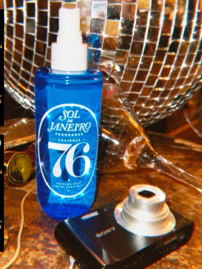 Sol de Janeiro Cheirosa '76 fragrance mist vessel adjacent to a achromatic Sony integer camera and a shiny, faceted solid entity connected a woody surface.